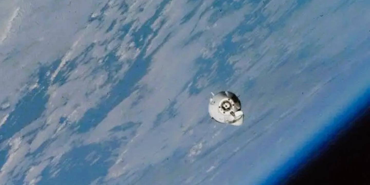 A small white space capsule orbits around the earth.