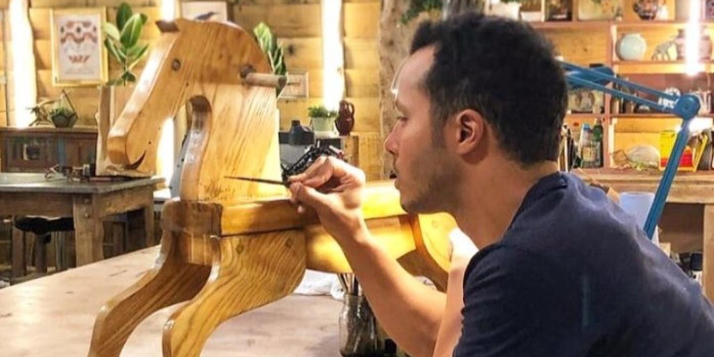 A restorer rest on his elbows while painting a wooden rocking horse.
