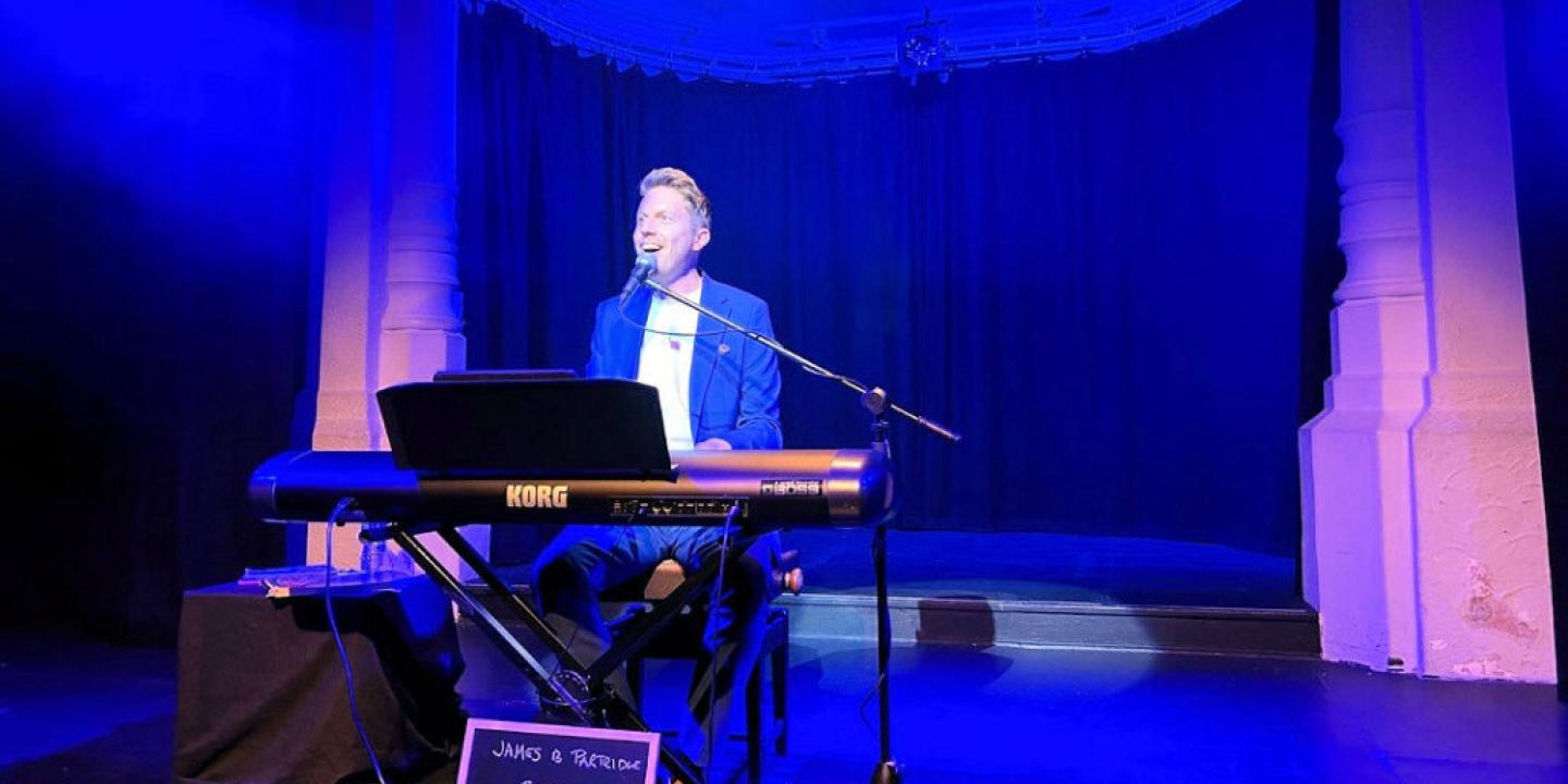 A pianist sits at a keyboard singing on a stage.