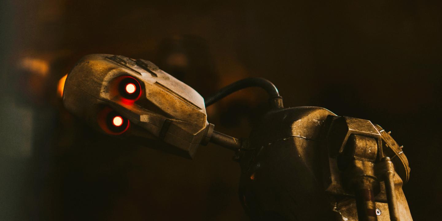 A tarnished humaniod robot rests its head to the side, its LED eyes look to the camera.