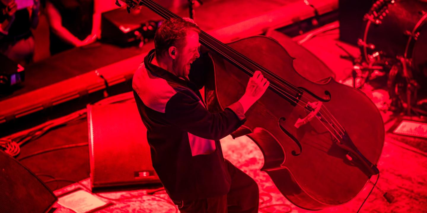 A bassist hauls a double bass of its base as he plays it.