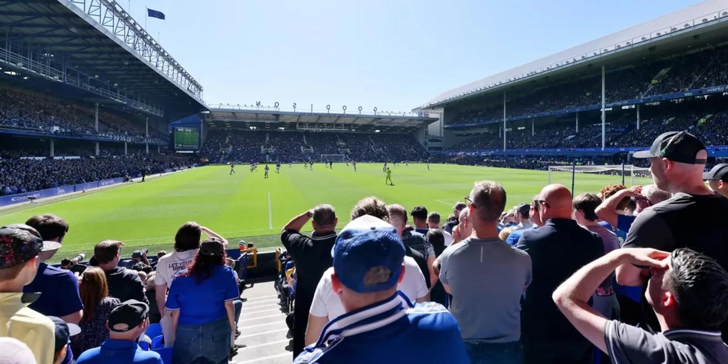 Football fans wearing blue stand and watch a match in a stadium.
