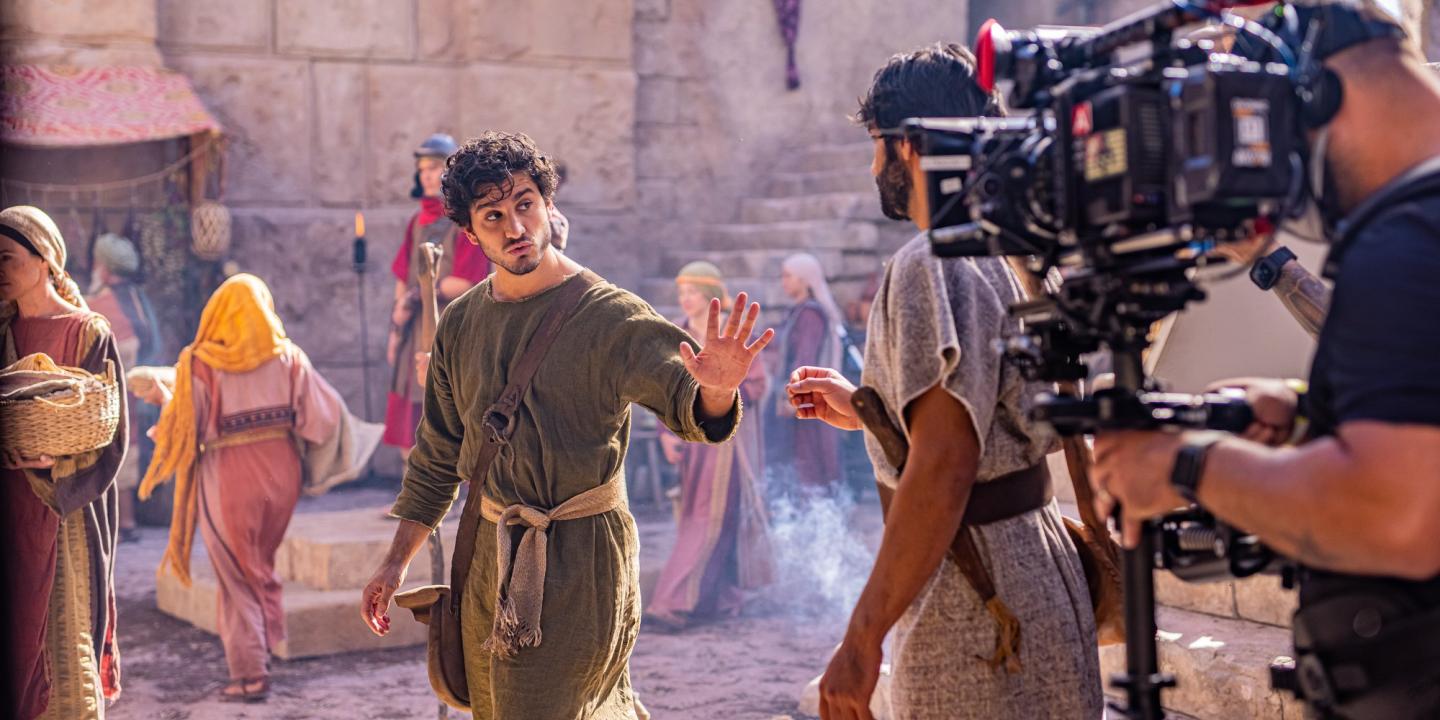 An actor dressed in an ancient Middle Eastern way is filmed by a large camera.