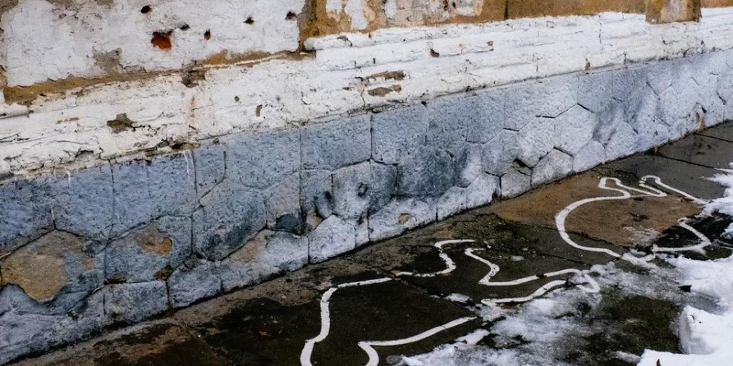 Bullet holes on a wall and white paint outlines mark the site of an execution