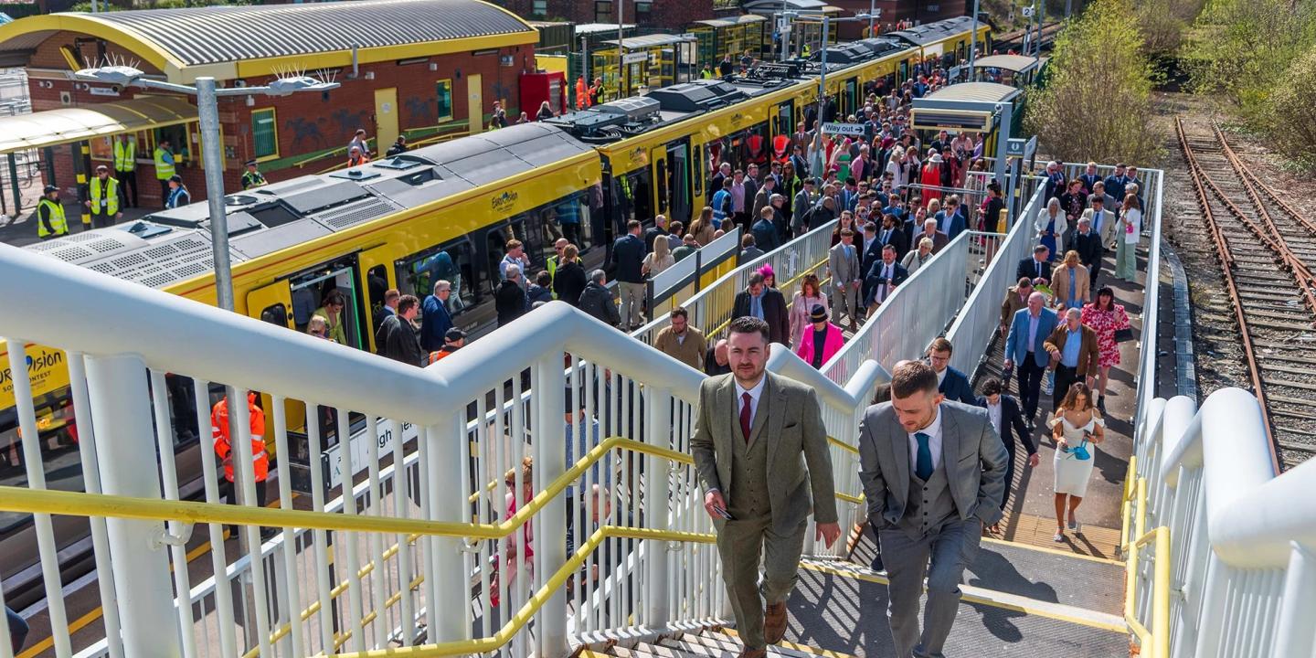 Smartly dressed people crowd a station platform and stairs.