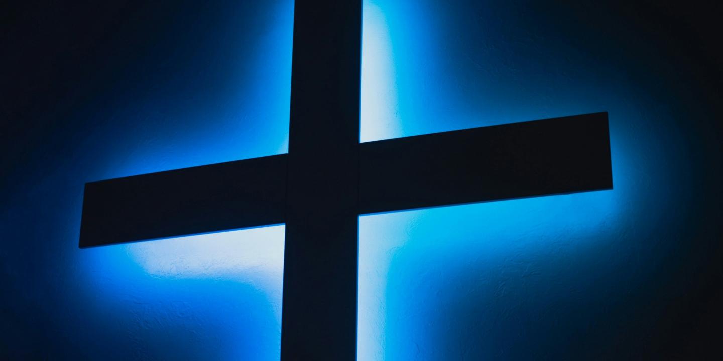 A black cross is backlit bya blue light.