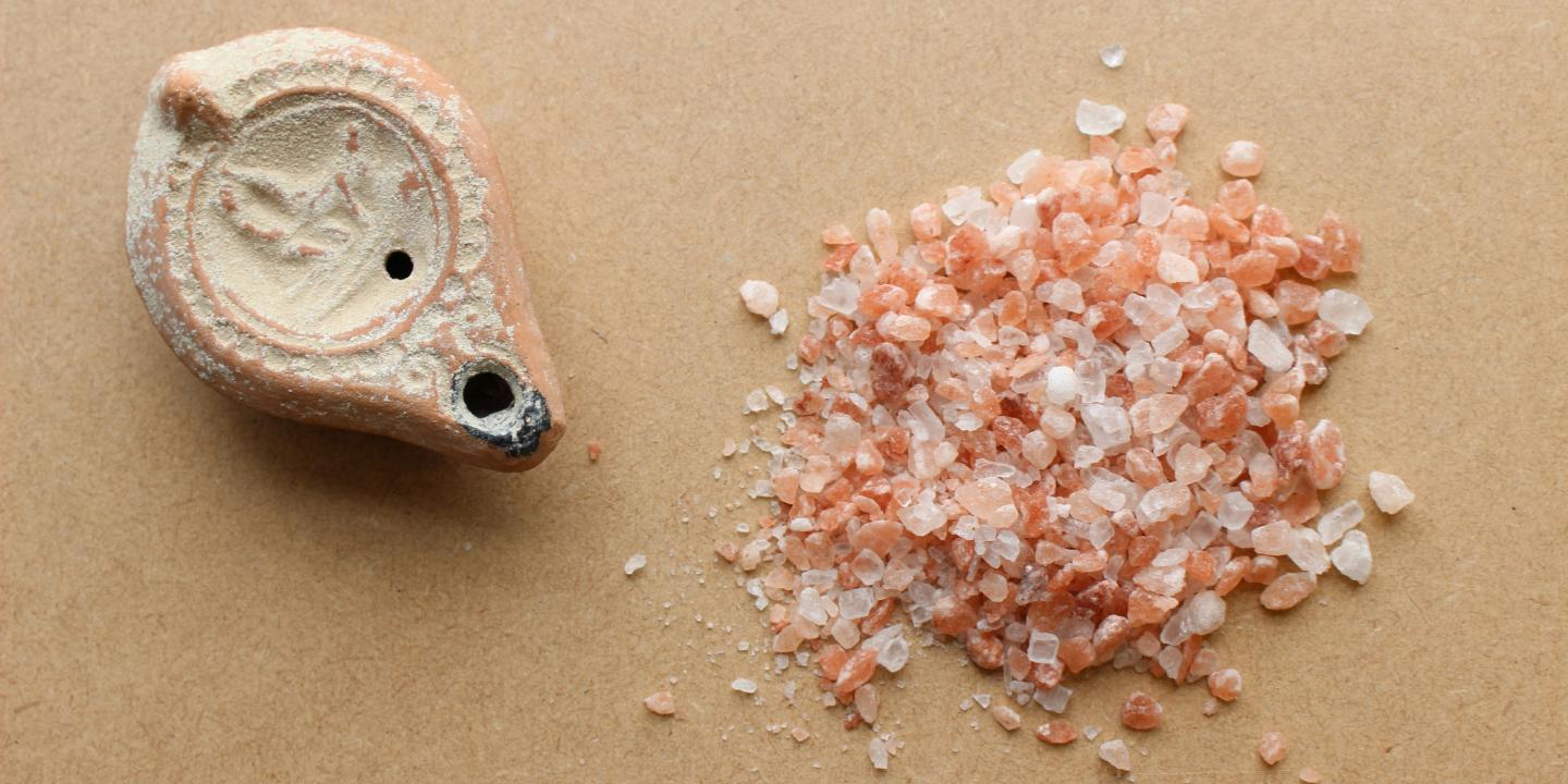An ancient salt shaker sits next to a pile of crushed rock salt.