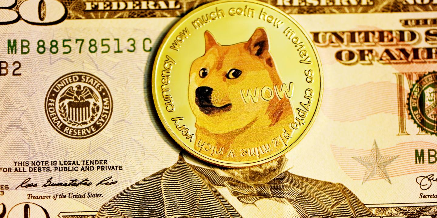 A gold coin with the DOGE dog on it, lies over the face on a $50 bill.