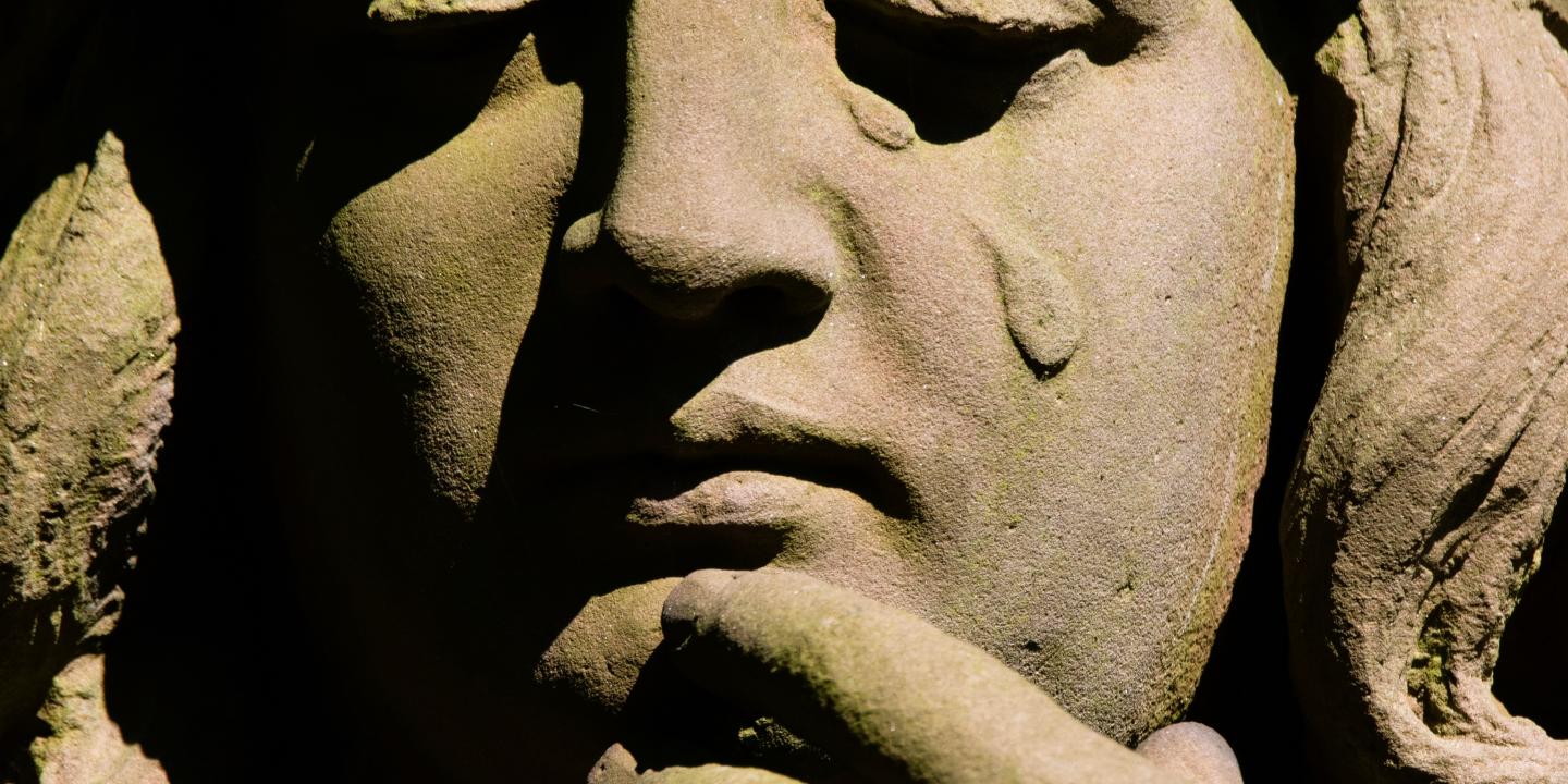 A stone statue's face depicts a falling tear.