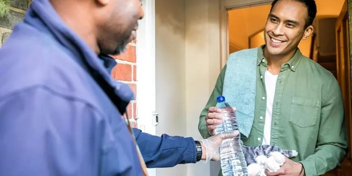 On a doorstep a man hands a bottle of water to another man.