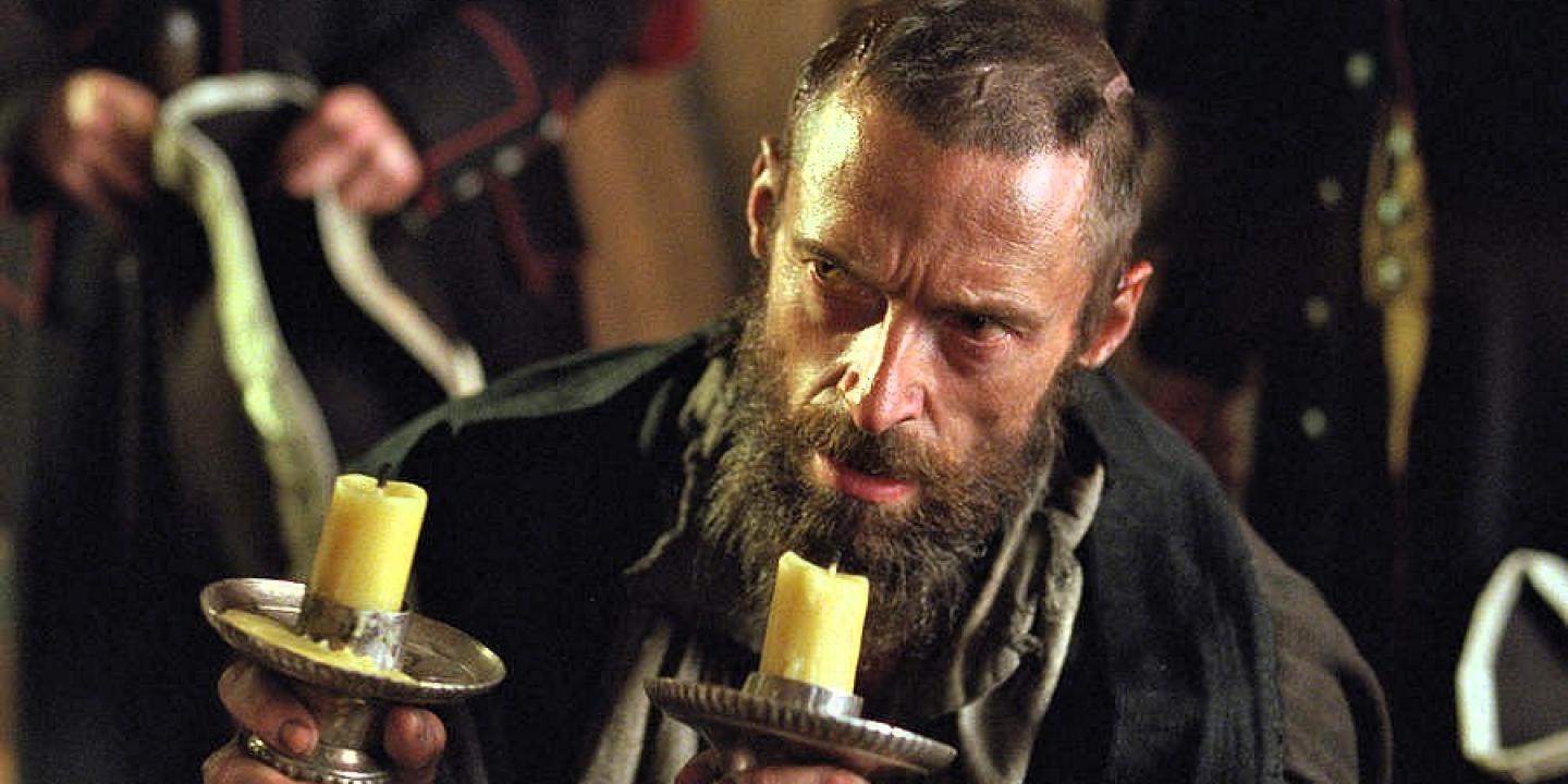 A desperate man wearing 18th century clothes holds candlesticks