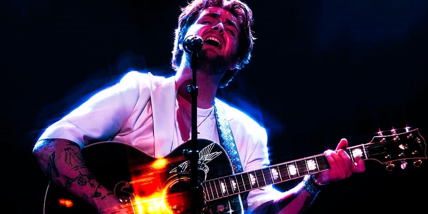 A singer holding a guitar raises his head with closed eyes.
