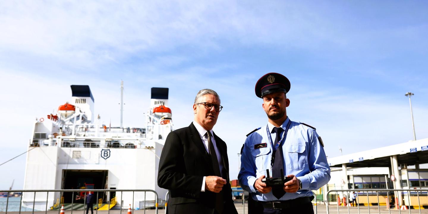 A prime minister stands next to an Albanian police officer in front of a ferry.
