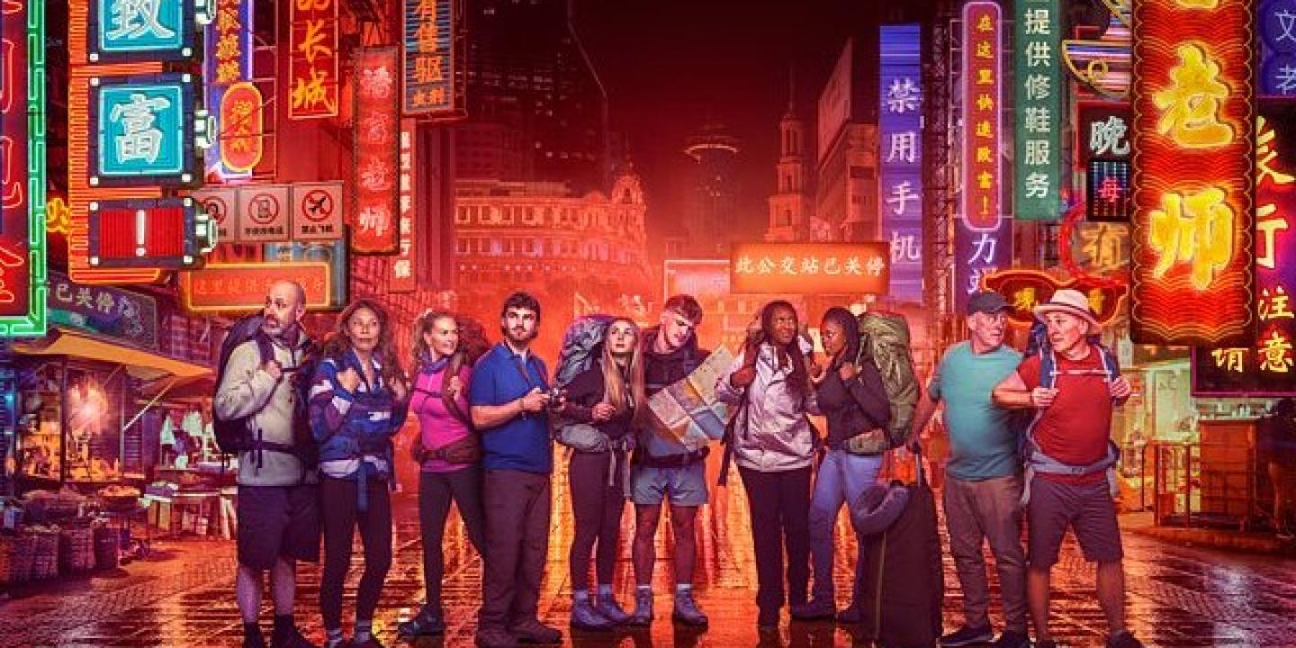 Contestants in Race Across the world stand in front of neon-lit Chinese street scene