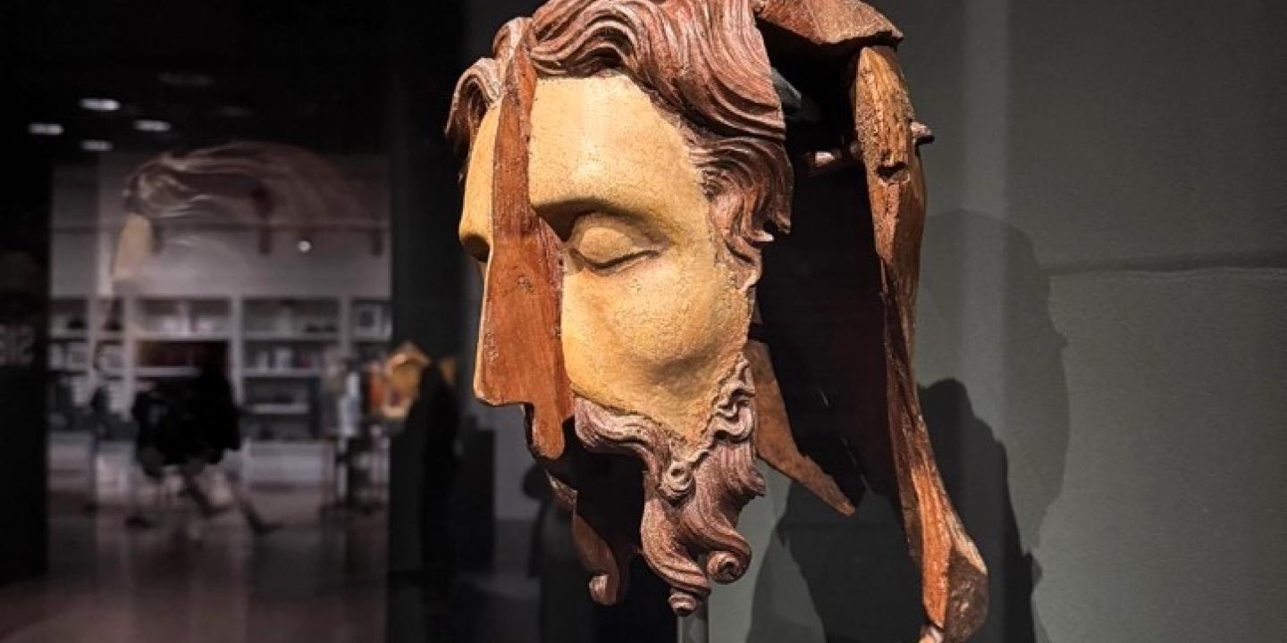 A split wooden sculpted head stands in an exhibition.