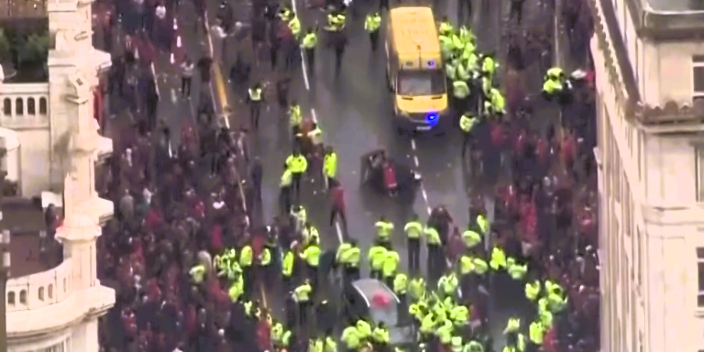 Aerial view of a yellow-jacketed police forming a cordon within a crowd.