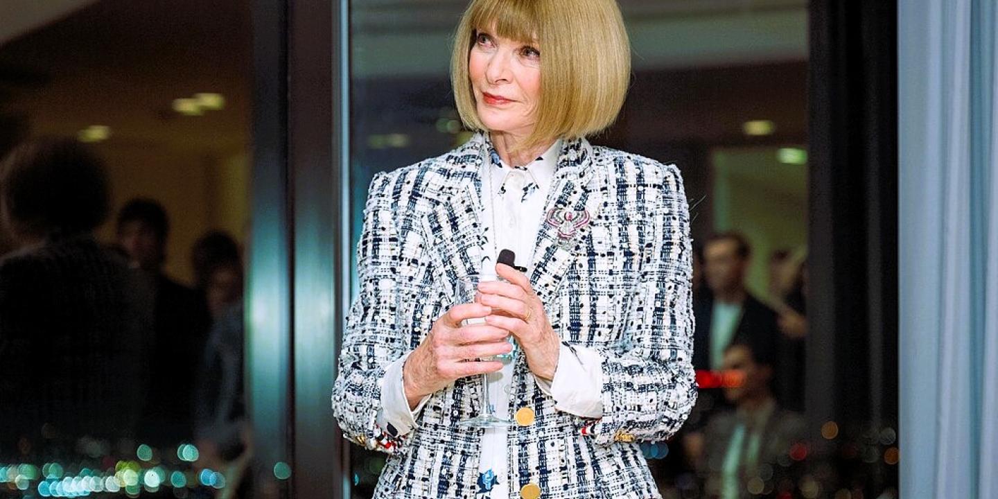Anna  Wintour stands holding a small mic.