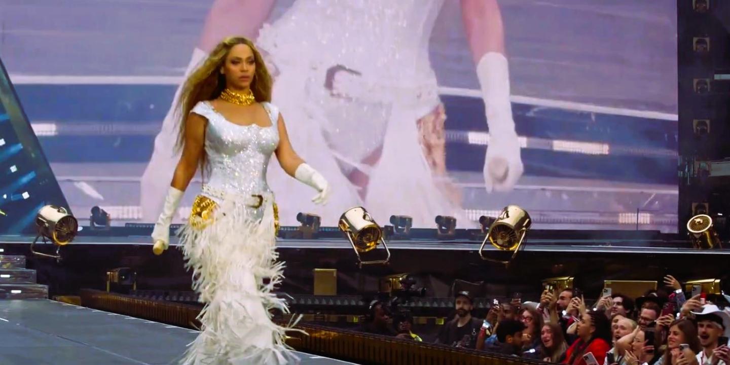 Beyonce marches along a stage catwalk as photographers stare from below.