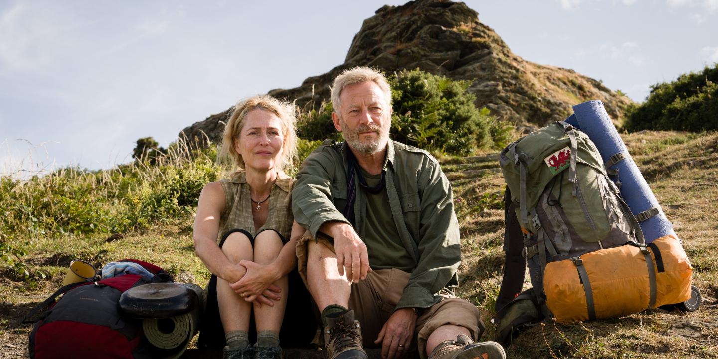A hiking couple sit on the grass next to a pack.