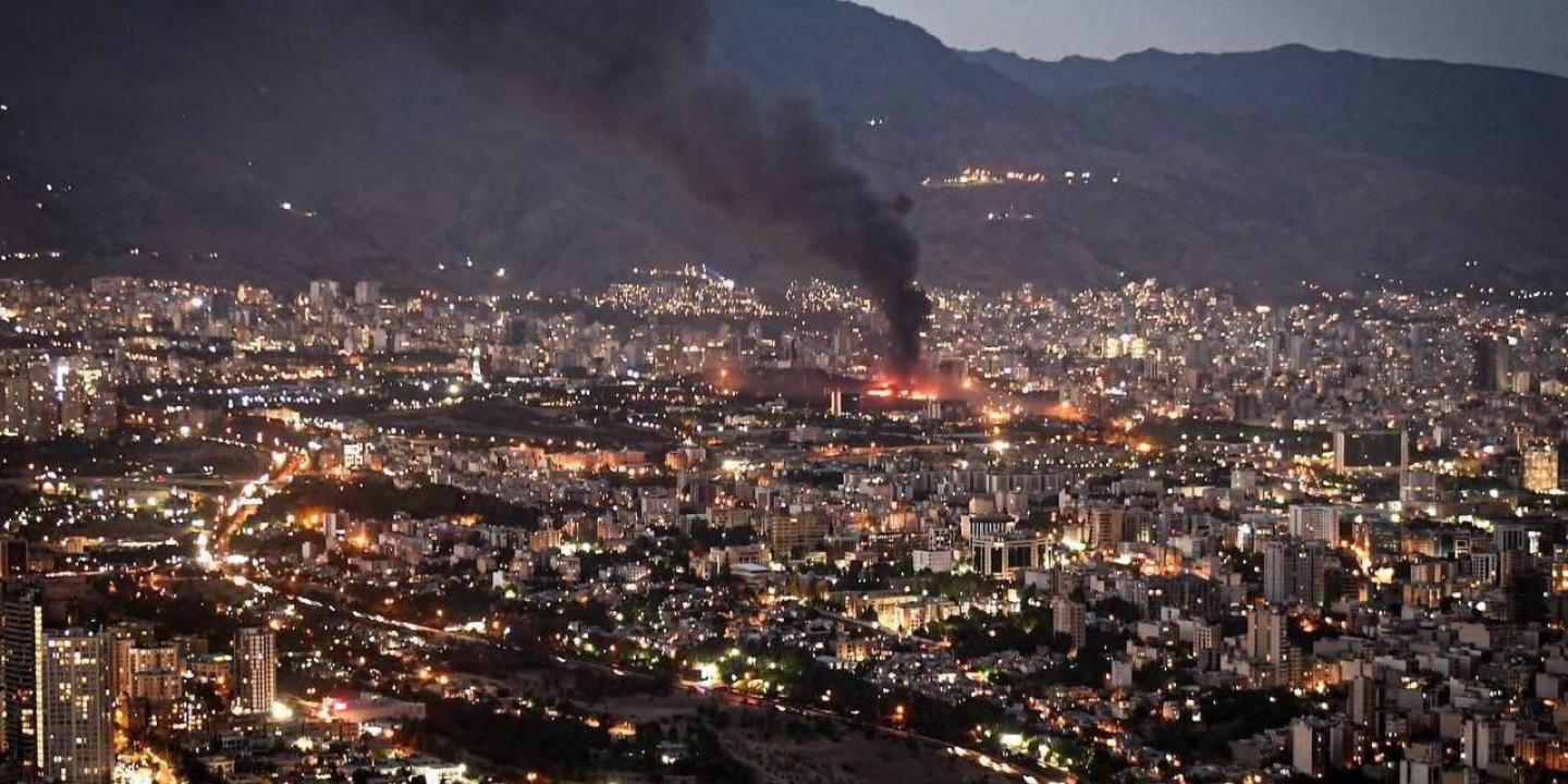 Smoke rises from the site of a bomb amid a high wide view of a city at twlight