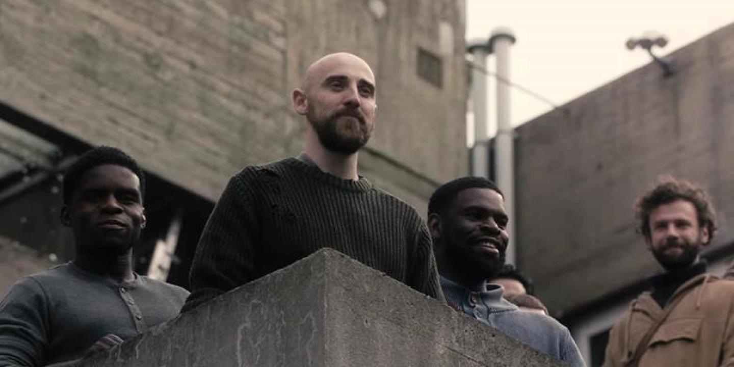 A man stands the landing of an external staircase and stares out.