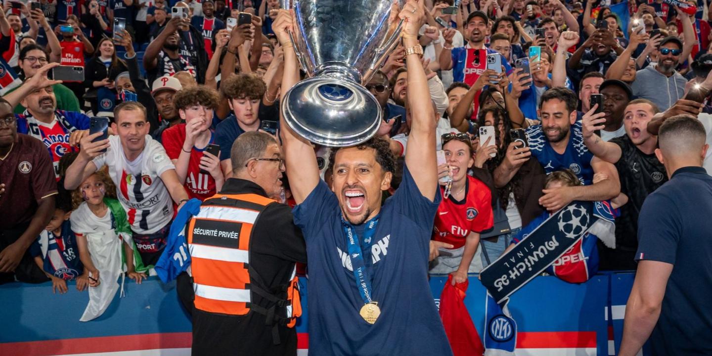 A footballer holds up the European cup, behind him fans are jubillant.