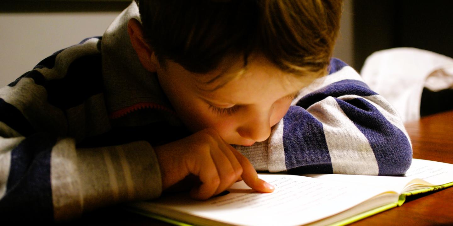 A young boy pores over a book tracing the lines with a finger.