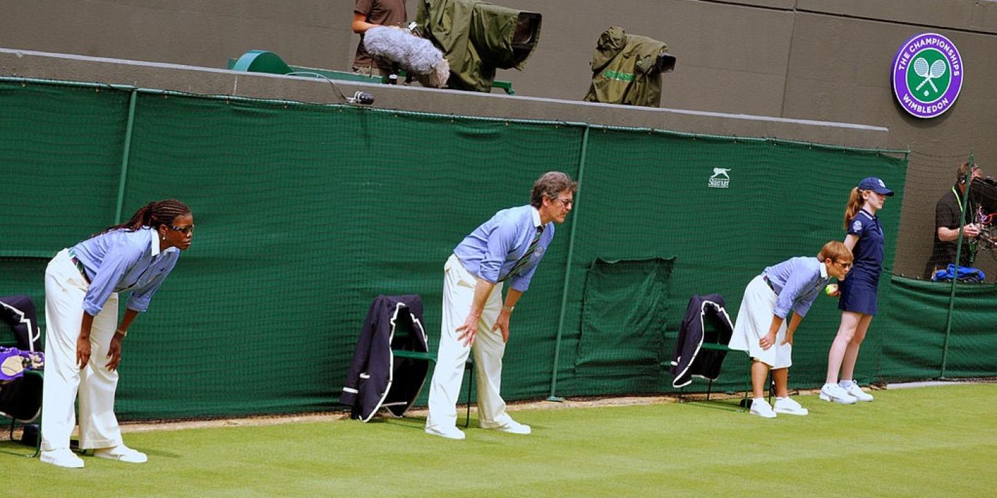 Tennis line judges stand and lean forward with hands on knees