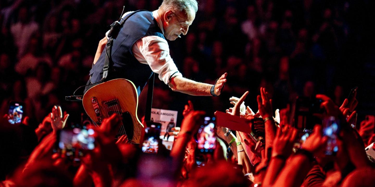 Bruce Springsteen crouches down and holds a hand out to a sea of outstretched hands