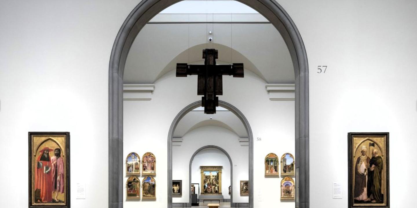 An art gallery arch reveals a suspended crucifix and other paintings in a distant room