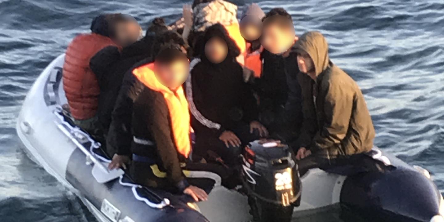 A people sumggler steers an overcrowded small boat.