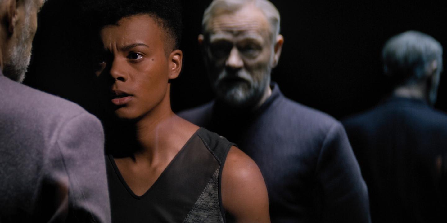 A woman confronts a man whose clone stands behind her.