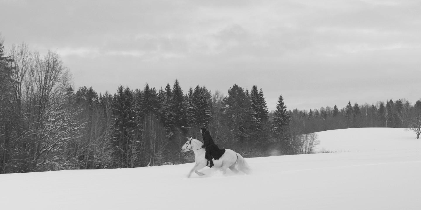 A nun on a white horse, gallops across a snowy field, in black and white