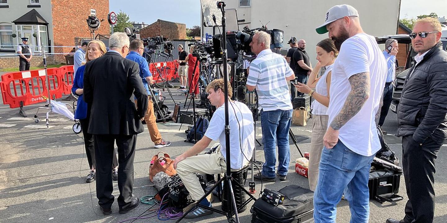 A media pack await a press conference in a street.