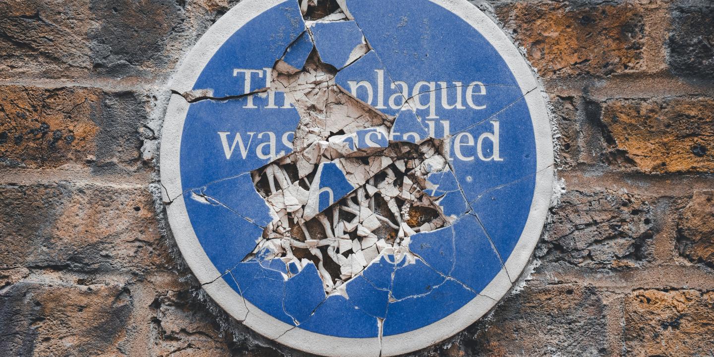 A commemorative blue plaque on a a wall is smashed to pieces