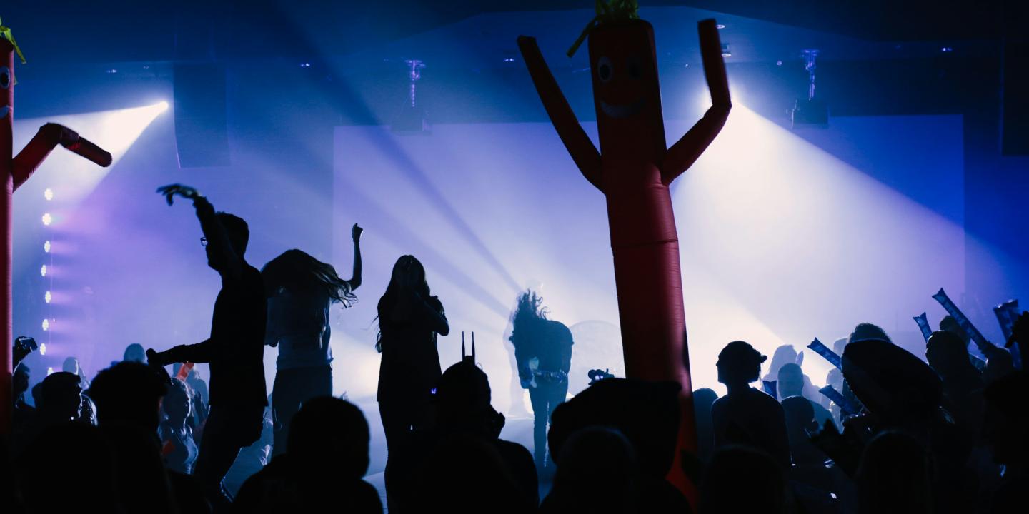 A band and audience are back lit against a stage.