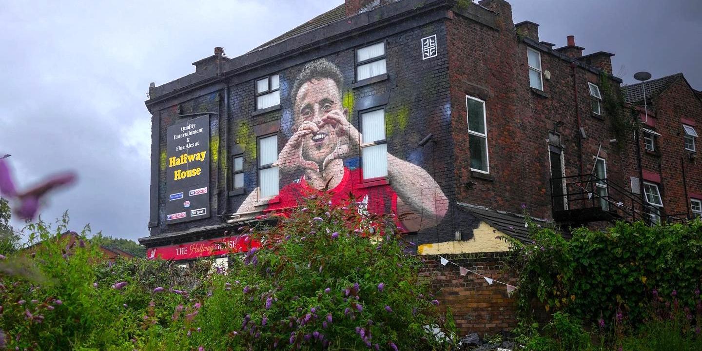A mural on a side of a pub shows a footballer making a heart sign.