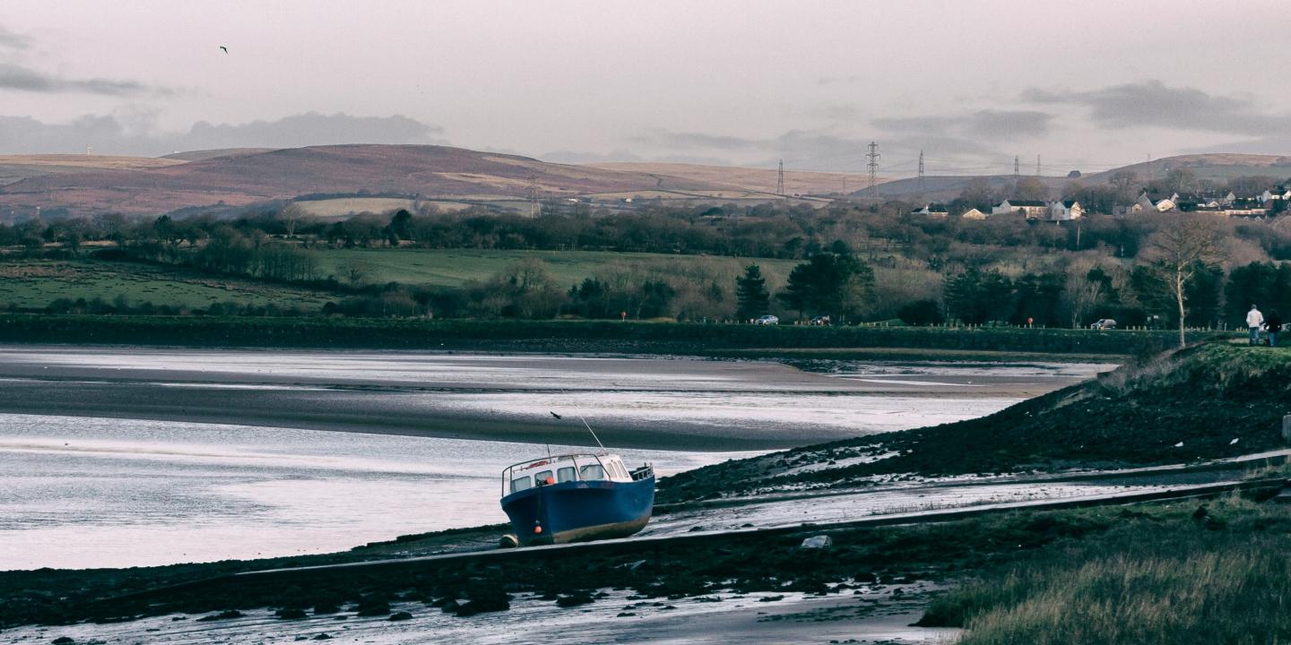 A boat rests on a mud bank of a river, hills are in the background.