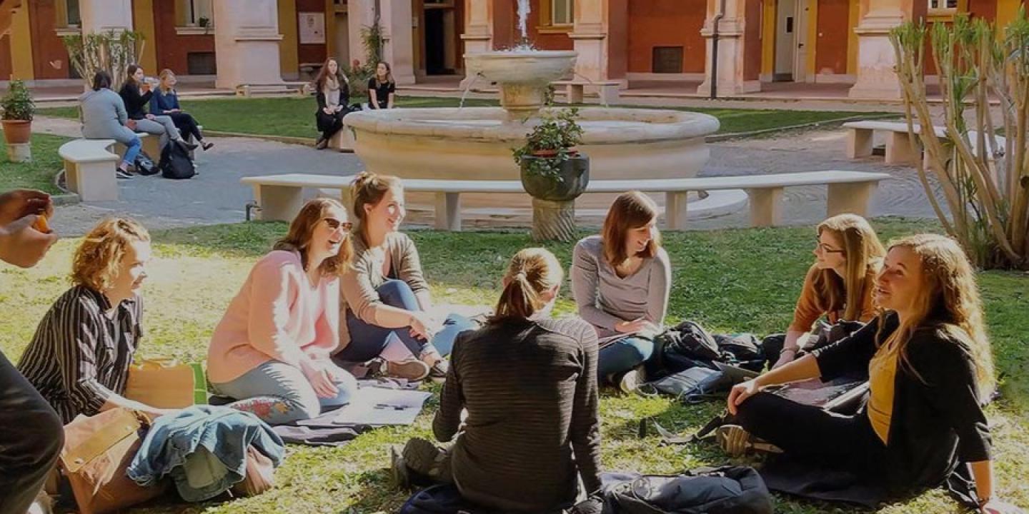 Students sit on the grass in front of a fountain.