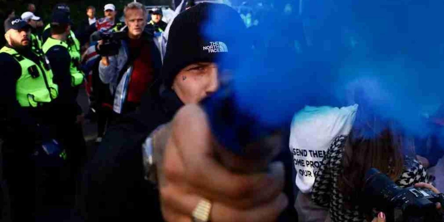 A protestor holds a blue smoke canister towards the camera lens.