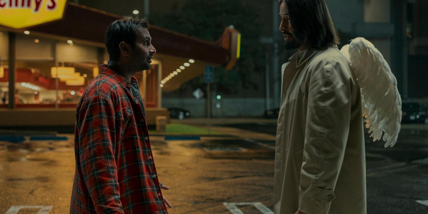 A film character talks to an angel in the street who has wings on the back of his coat.