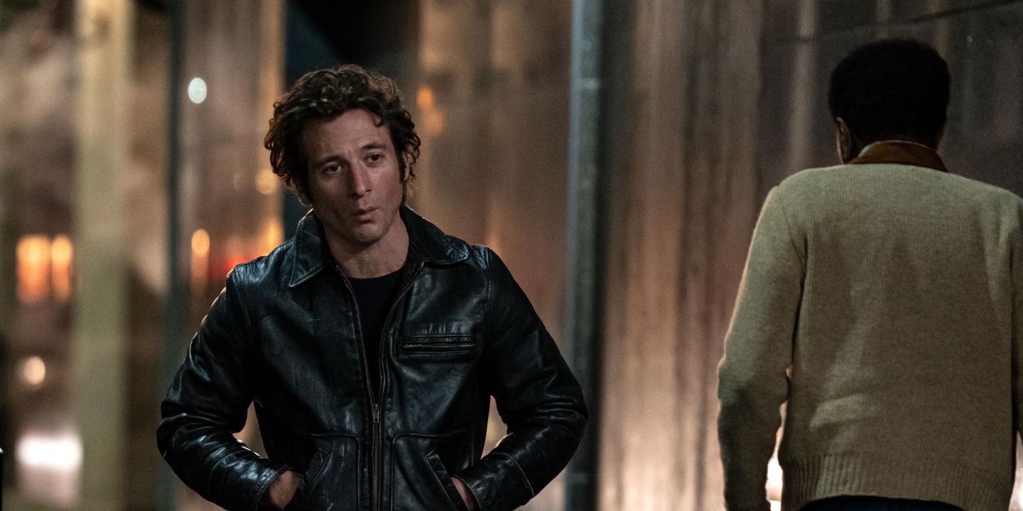 An actor playing Bruce Springsteen walks down a dark street, hands in jacket pocket.