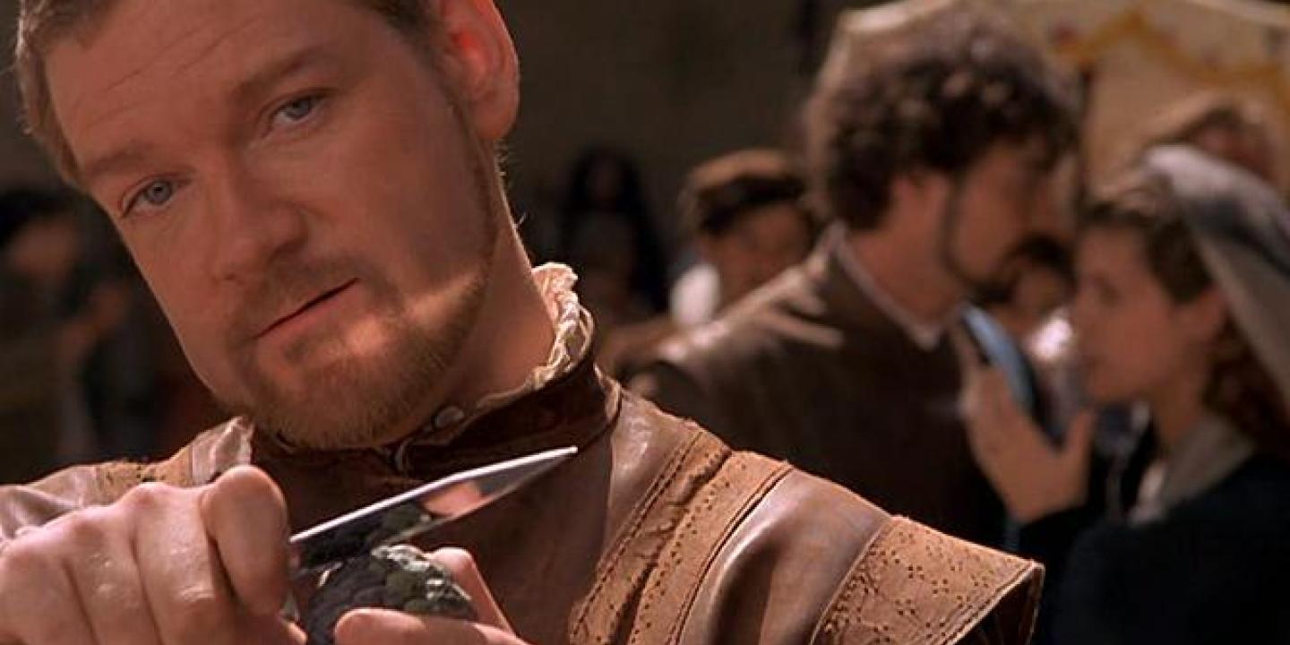 An Elizabethan man holds a dagger up while grinning.