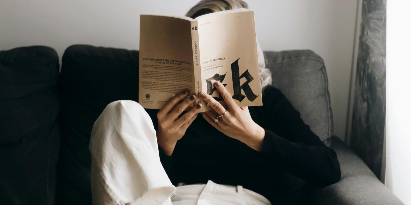   A reader sits on a sofa with a raised leg and holds a book