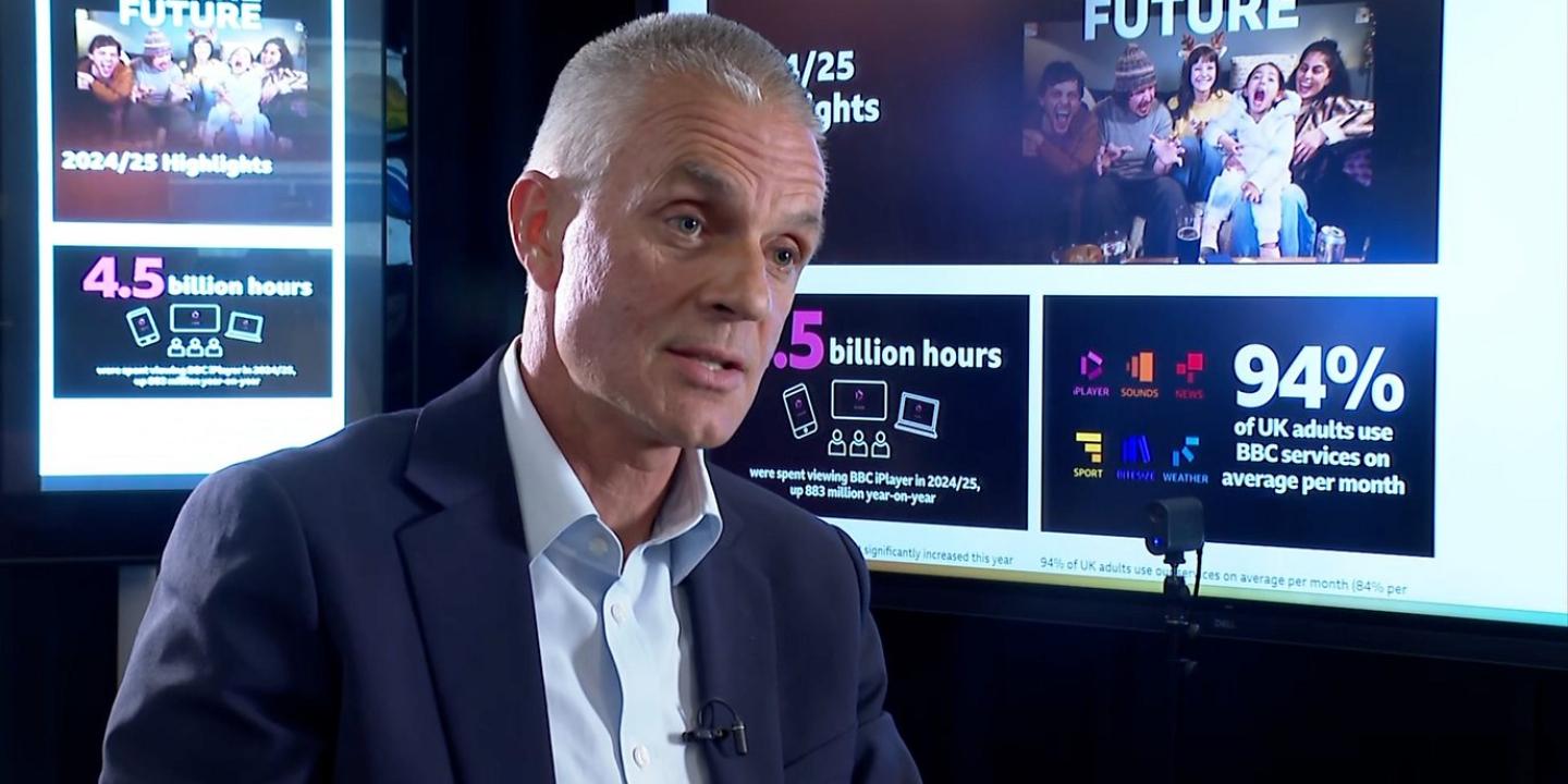 TIm Davie, sits in an interview in front of screens showing facts about the BBC