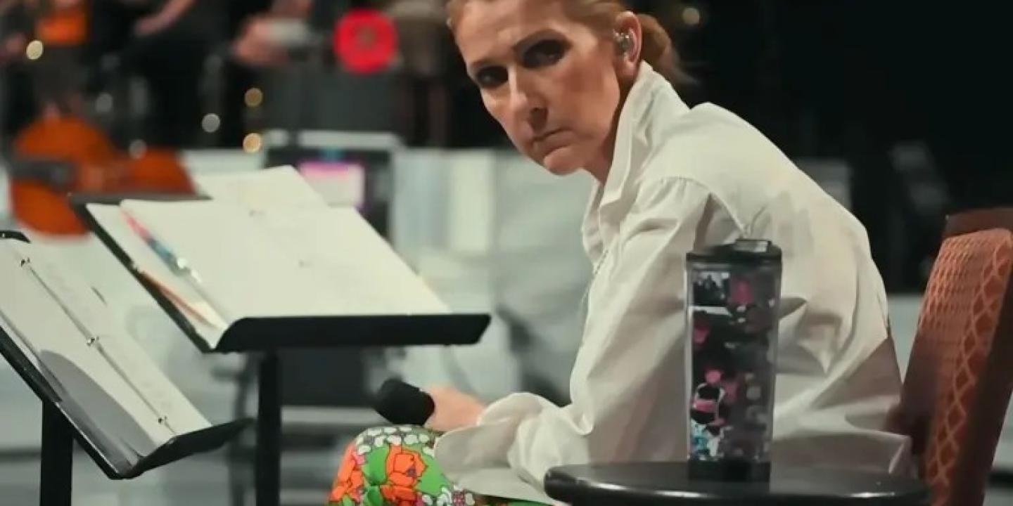 A seated Celine Dion, leans forward, head to the side, holding a mic.