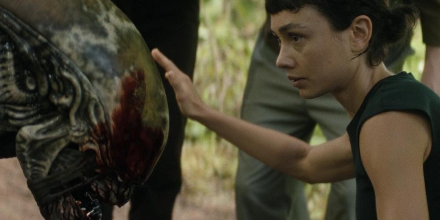 A young woman pets the head of an alien