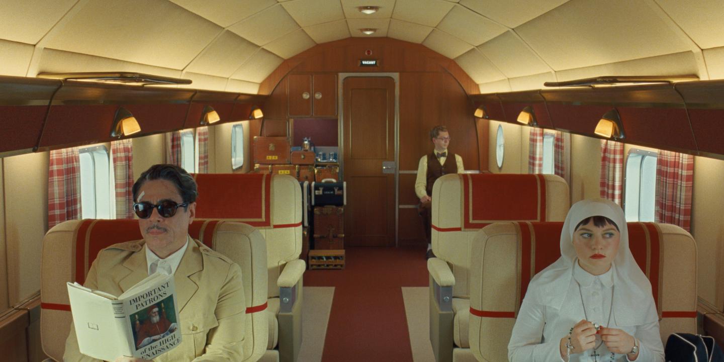 Characters from a Wes Anderson film sit in a stylish plane interior.