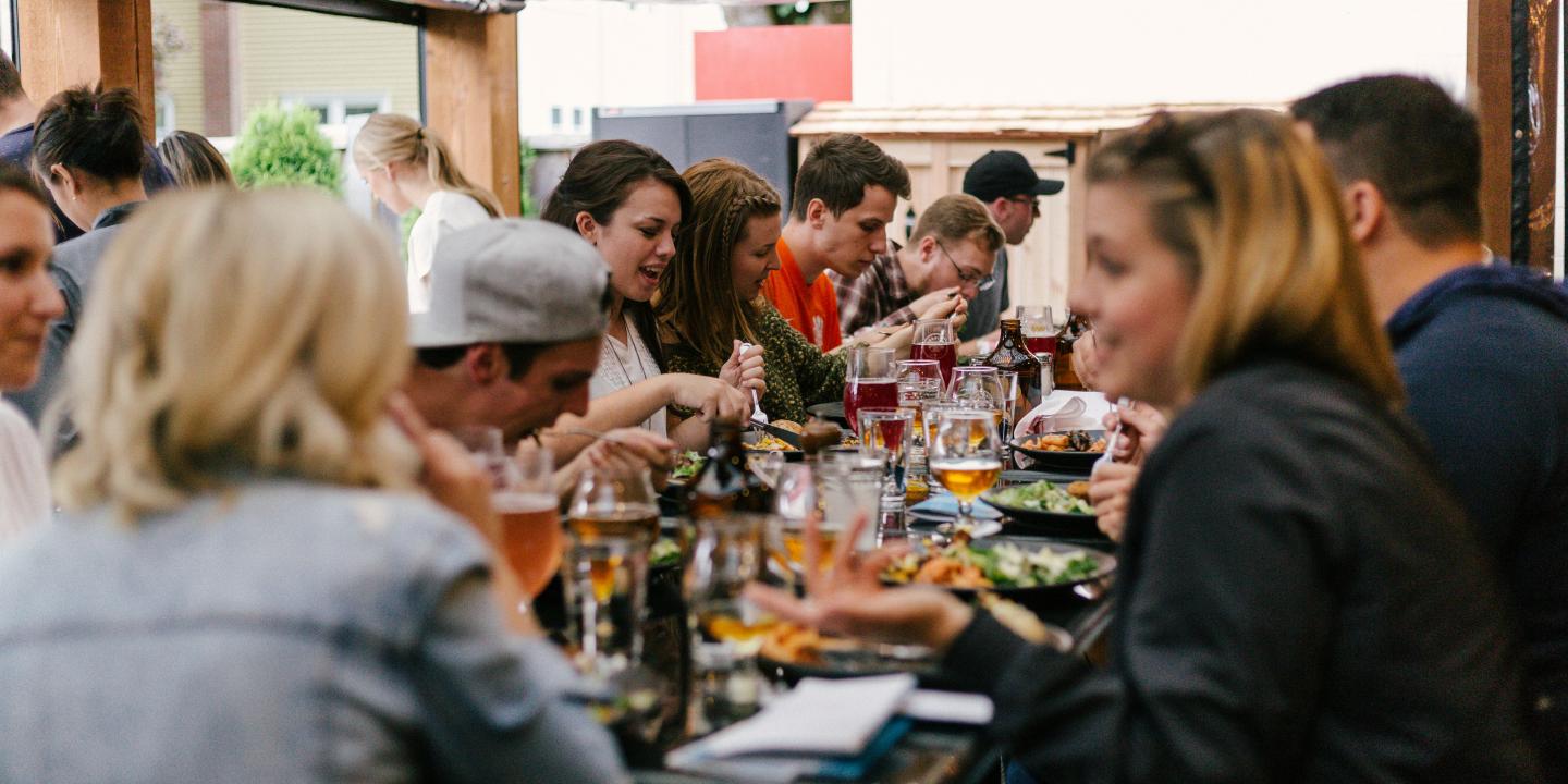 A group of friends sit arouns a large table eating together.