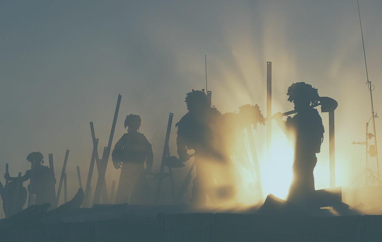 Soldiers silhouetted by dust and sunshine work at a fence with tools.
